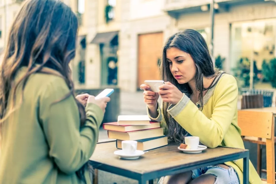 Deux adolescentes envoient des SMS en prenant un café.