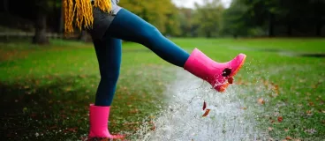 DIY d'automne : pour des bottes qui vous bottent ! Une femme vêtue de bottes de pluie saute dans des flaques d’eau
