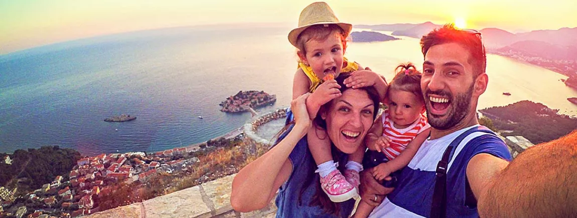 TOP 10 des accessoires indispensables pour des vacances réussies avec Maxwell House ! Des parents avec leurs deux enfants qui se prennent en selfie, en vacances, devant un paysage de rêve