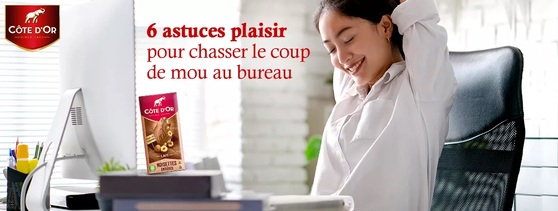 6 astuces plaisir pour chasser le coup de mou au bureau Une femme heureuse au bureau qui mange du chocolat
